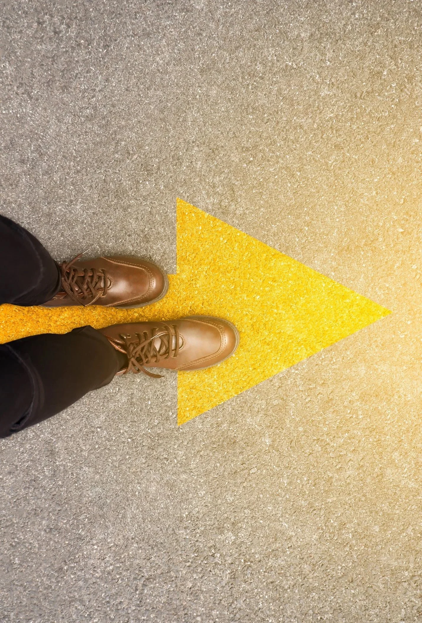 Feet standing on an arrow painted on pavement, representing moving forward